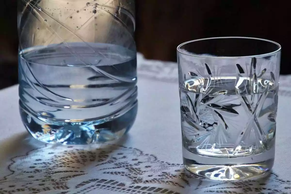 Una vaso de agua lleno junto a una botella medio vacía en una mesa