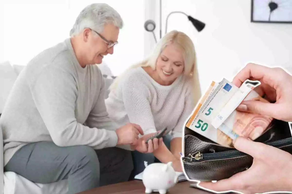 Una pareja mayor sonriente revisa sus finanzas en casa mientras una mano saca billetes de euro de una cartera.