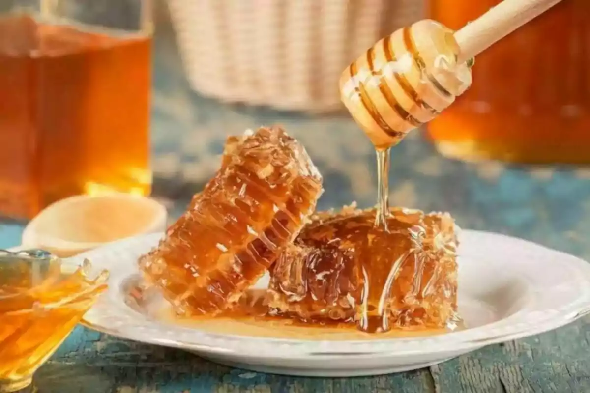 Panales de miel en un plato con miel líquida siendo vertida desde un cucharón de madera.