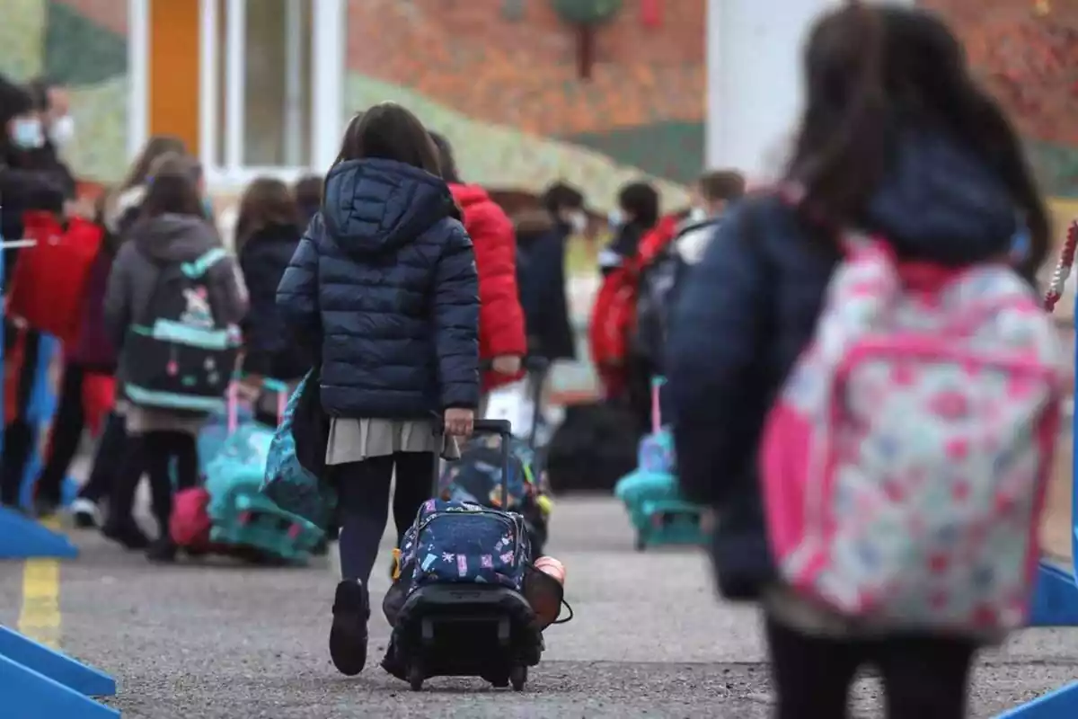 Imagen de varios niños en el exterior de una escuela entrando con sus mochilas